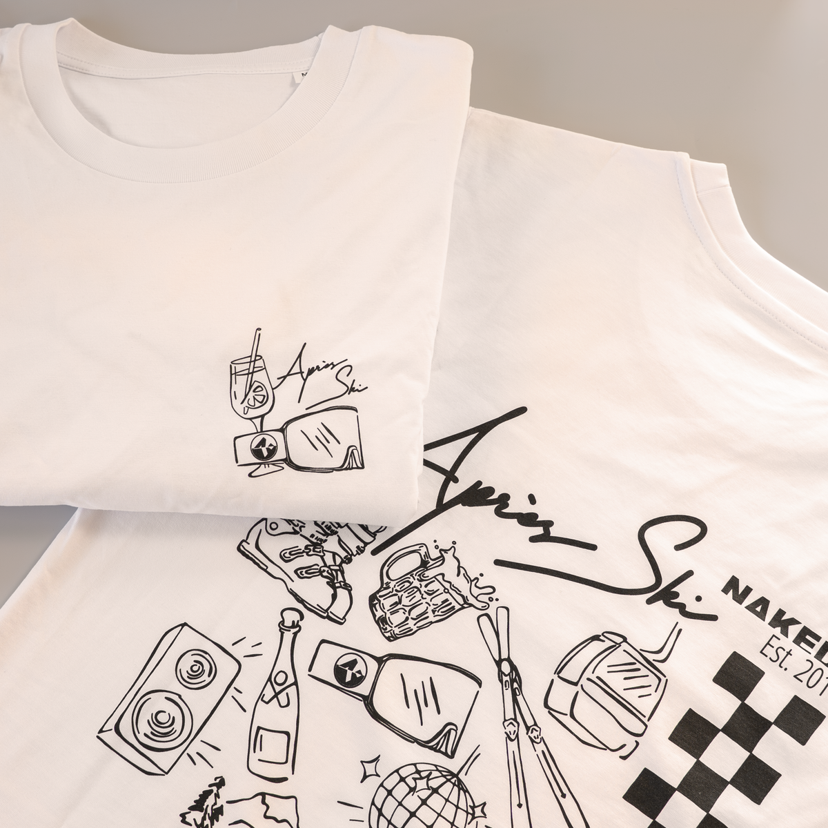 Due magliette bianche “Langarm Shirt - Apres” di NAKED Optics, realizzate in cotone biologico, presentano disegni al tratto neri raffiguranti sci, bevande, altoparlanti e altri motivi ispirati al mondo delle feste. La divertente stampa sul retro “Party Back Print” cattura perfettamente lo spirito dell’après-ski in uno stile disinvolto.