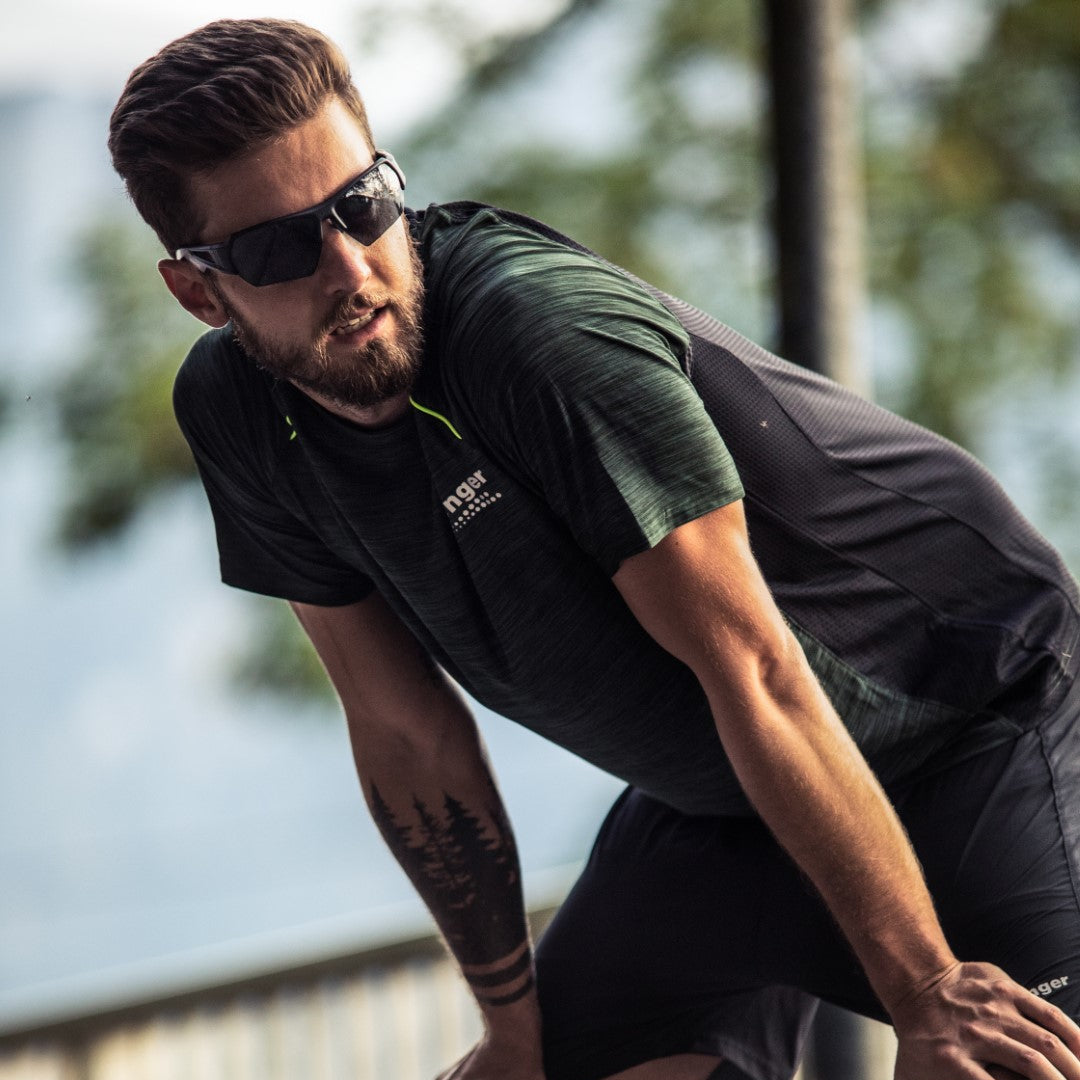 A man in NAKED Optics’ The CHARGE Halfframe sunglasses and athletic wear leans forward outdoors, appearing to take a break from exercising. The ultralight UV400 sportbrille provides comfort and protection during intense activity.