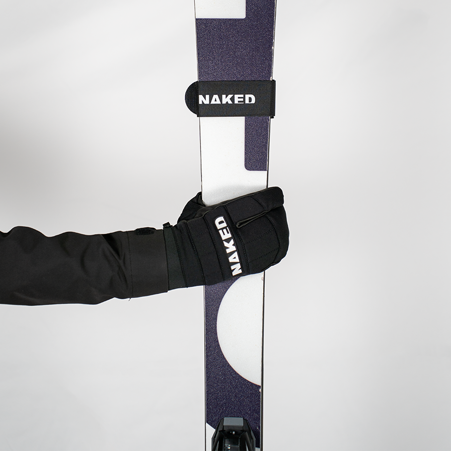 Eine Hand in einem Handschuh hält All-Mountain-Ski, die mit NAKED Optics Ski-Strap (Skifix)-Gurten befestigt sind, vor einem schlichten weißen Hintergrund.