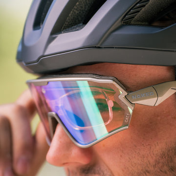 Nahaufnahme einer Person, die einen schwarzen Fahrradhelm und eine reflektierende Sonnenbrille mit der Aufschrift „NAKED“ auf dem Rahmen trägt. Zu sehen ist das „Optisches Insert HAWK“ von NAKED Optics – eine Sportbrille, die dank ihres innovativen optischen Einsatzes auf die individuelle Sehstärke abgestimmt werden kann.