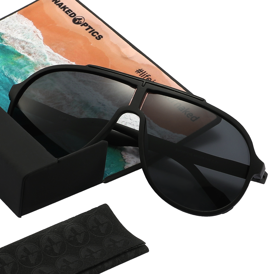 The PILOT sunglasses by NAKED Optics, featuring an oversized design and UV400 dark lenses, rest on their case atop a postcard depicting a stunning beach and ocean scene.