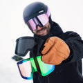 Eine Person in Skikleidung hält an einem verschneiten Tag zwei Paar NAKED Optics Ersatzglas SOLAR-Skibrillen hoch, eine schwarze und eine grüne, die jeweils mit Magnetwechselglas und einer Anti-Fog-Beschichtung ausgestattet sind.