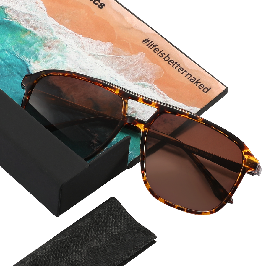 Tortoiseshell sunglasses with brown lenses rest on a box, accompanied by a beach postcard and the visible hashtag #lifeisbetternaked—these “The CARTEL” sunglasses from NAKED Optics feature a classic retro design, making them perfect for sunny days.