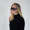 Woman with long blonde hair wearing NAKED Optics The PILOT UV400 black sunglasses and a black turtleneck against a plain background.