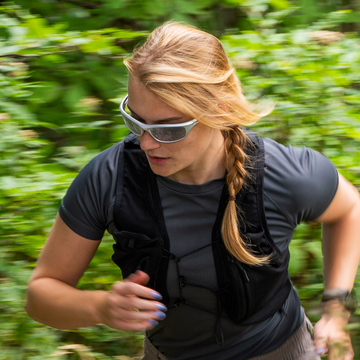 Runner wearing white NAKED Optics RAVE sports sunglasses on a wooded trail.