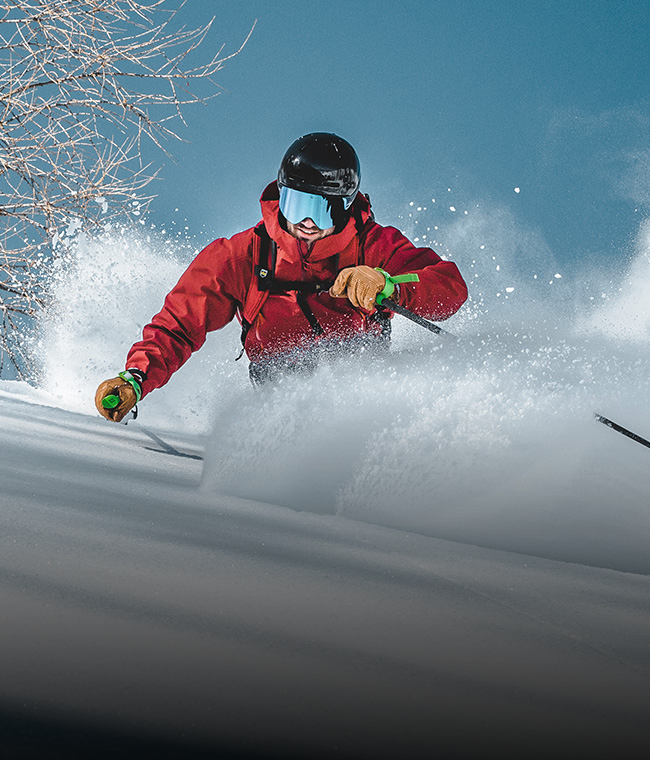 Ein Skifahrer in roter Jacke und mit Helm gleitet an einem sonnigen Tag zügig durch den Pulverschnee.