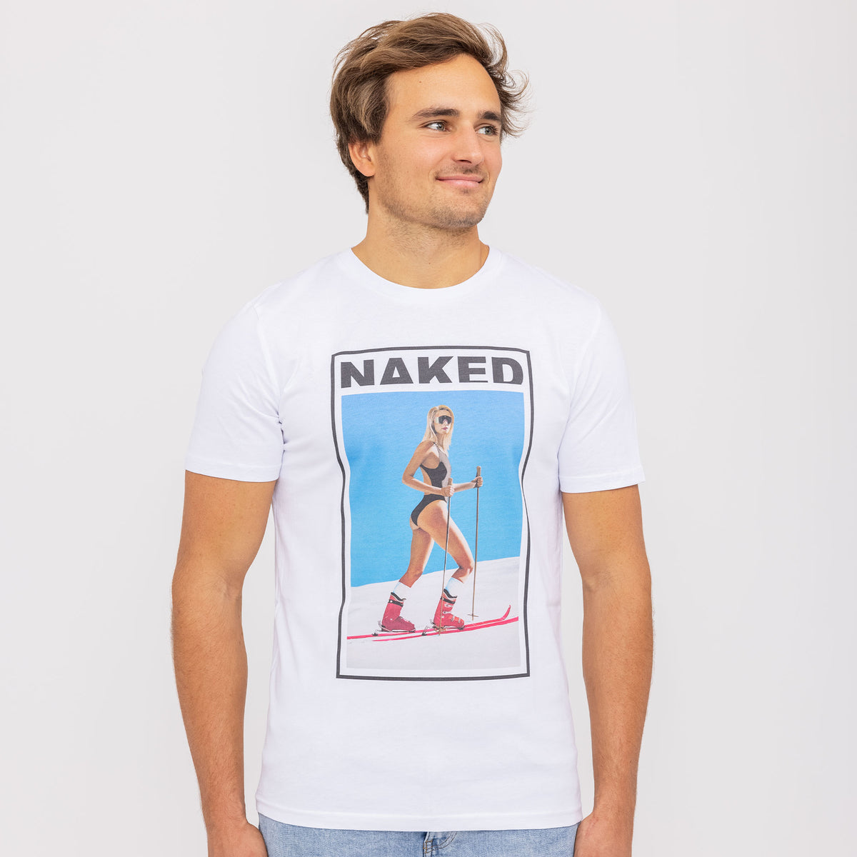 A man wearing a white NAKED Optics T-Shirt Skiing-Girl featuring a graphic of a woman skiing in swimwear on the front, characterized by its unique design and made from Fair Wear organic cotton.