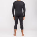 Ein Mann, der die NAKED Optics Thermo-Unterwäsche für Herren (100 % Merino) trägt, steht barfuß in einem dunklen Langarmshirt und passenden Leggings mit dem Rücken zu einem schlichten weißen Hintergrund und unterstreicht so die schlanke Passform dieser nahtlosen Funktionsunterwäsche aus Merinowolle.
