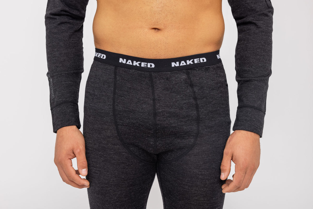 Eine Person trägt schwarze Thermo-Unterwäsche für Herren (100 % Merino) von NAKED Optics, deren Bund den Markennamen „NAKED“ in weißen Buchstaben trägt. Der Oberkörper ist zu sehen, wodurch diese stilvolle Merino-Unterwäsche für Herren, die auf maximalen Komfort ausgelegt ist, besonders gut zur Geltung kommt.