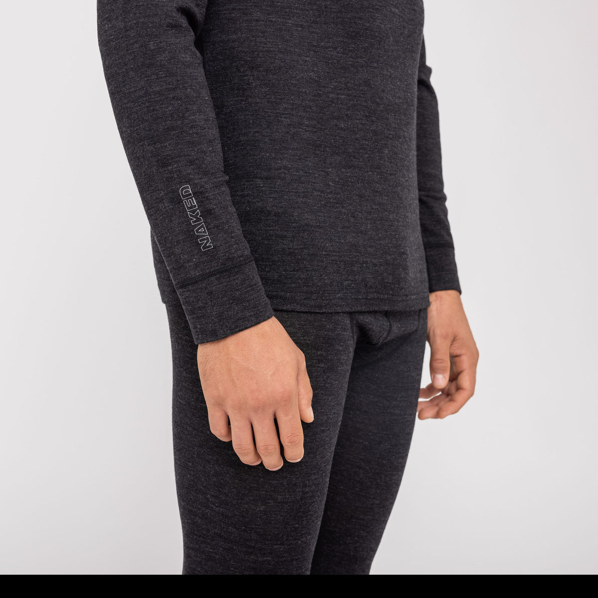 Si vede una persona che indossa l'intimo termico da uomo NAKED Optics (100% lana merino), composto da una maglia termica a maniche lunghe di colore scuro e da pantaloni abbinati; sono visibili solo il busto e le braccia. Questo completo aderente mette in risalto l’intimo funzionale in lana merino senza cuciture, che garantisce calore e traspirabilità eccezionali, rendendolo ideale per essere indossato a strati.