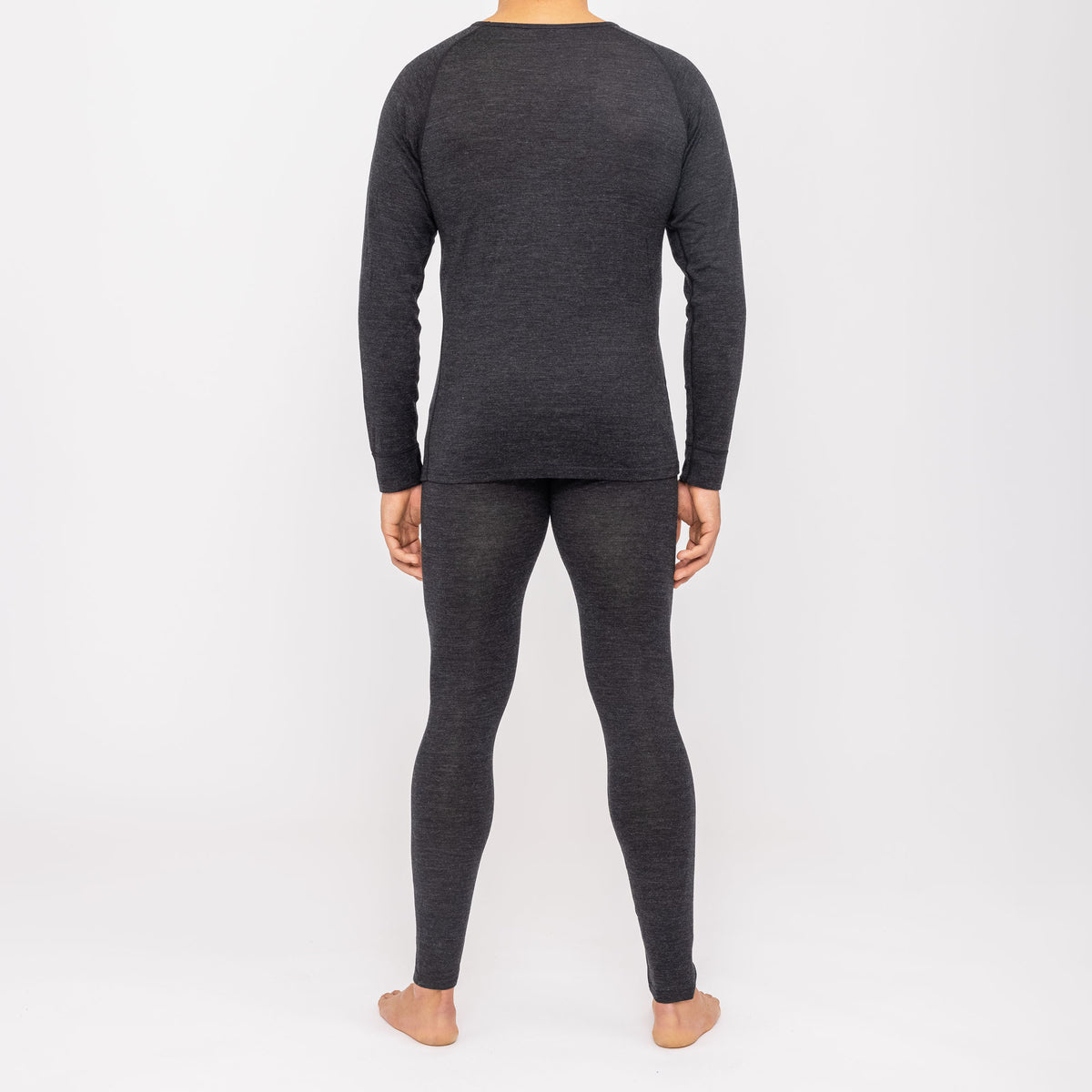 Una persona è in piedi a piedi nudi, di spalle, e indossa un completo coordinato composto da una maglia a maniche lunghe scura e da leggings della linea NAKED Optics Thermo-Unterwäsche Herren (100% lana merino).