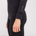 A person is wearing NAKED Optics Thermo-Unterwäsche Damen (100% Merino), featuring a dark long-sleeve top and leggings made from soft Merino wool, with “NAKED” written on the sleeve. Their hand is relaxed.
