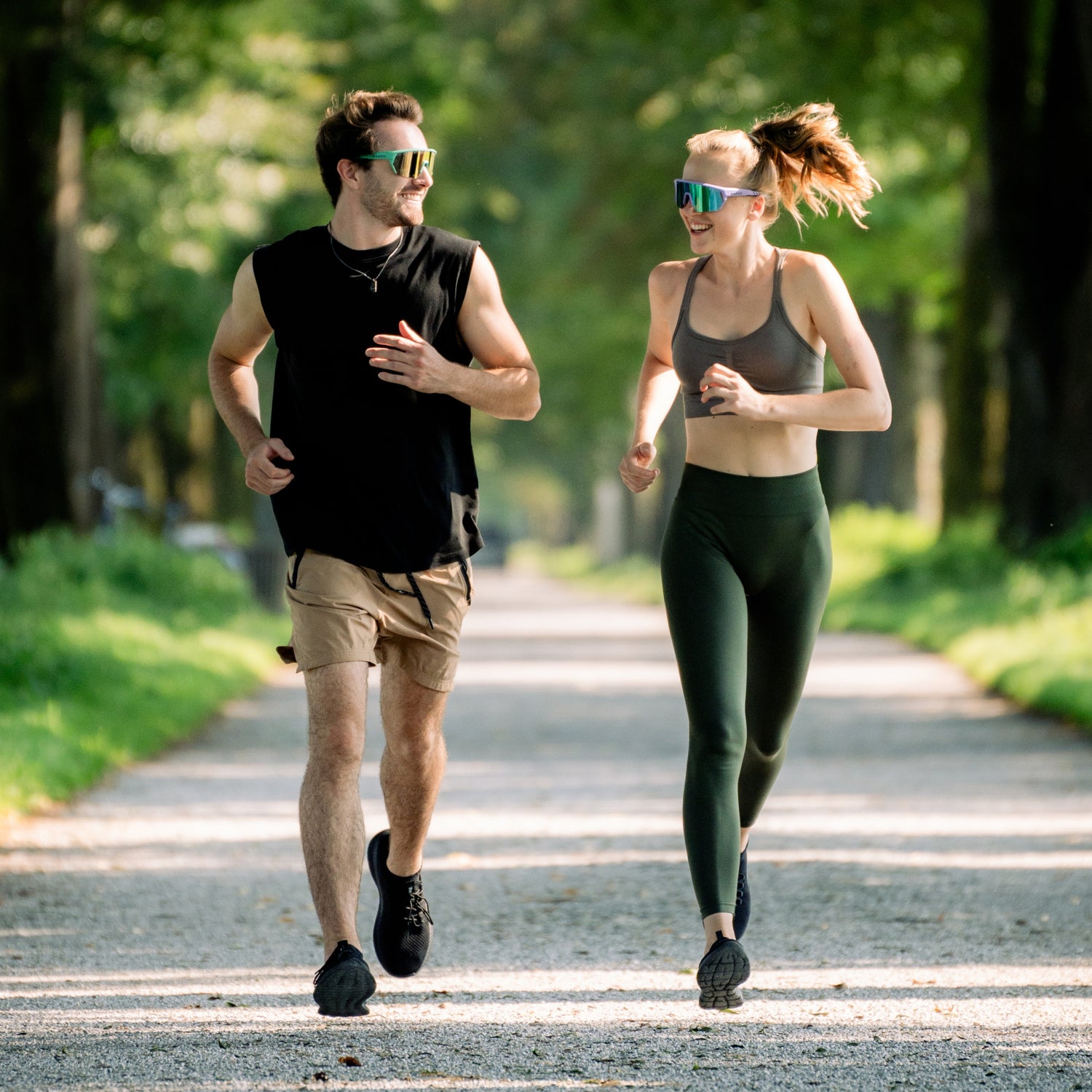 Ein junges Paar läuft gemeinsam auf einem Shotterweg, sie tragen bunte Sportbrillen und lachen sich an; Credits: Elias Neier