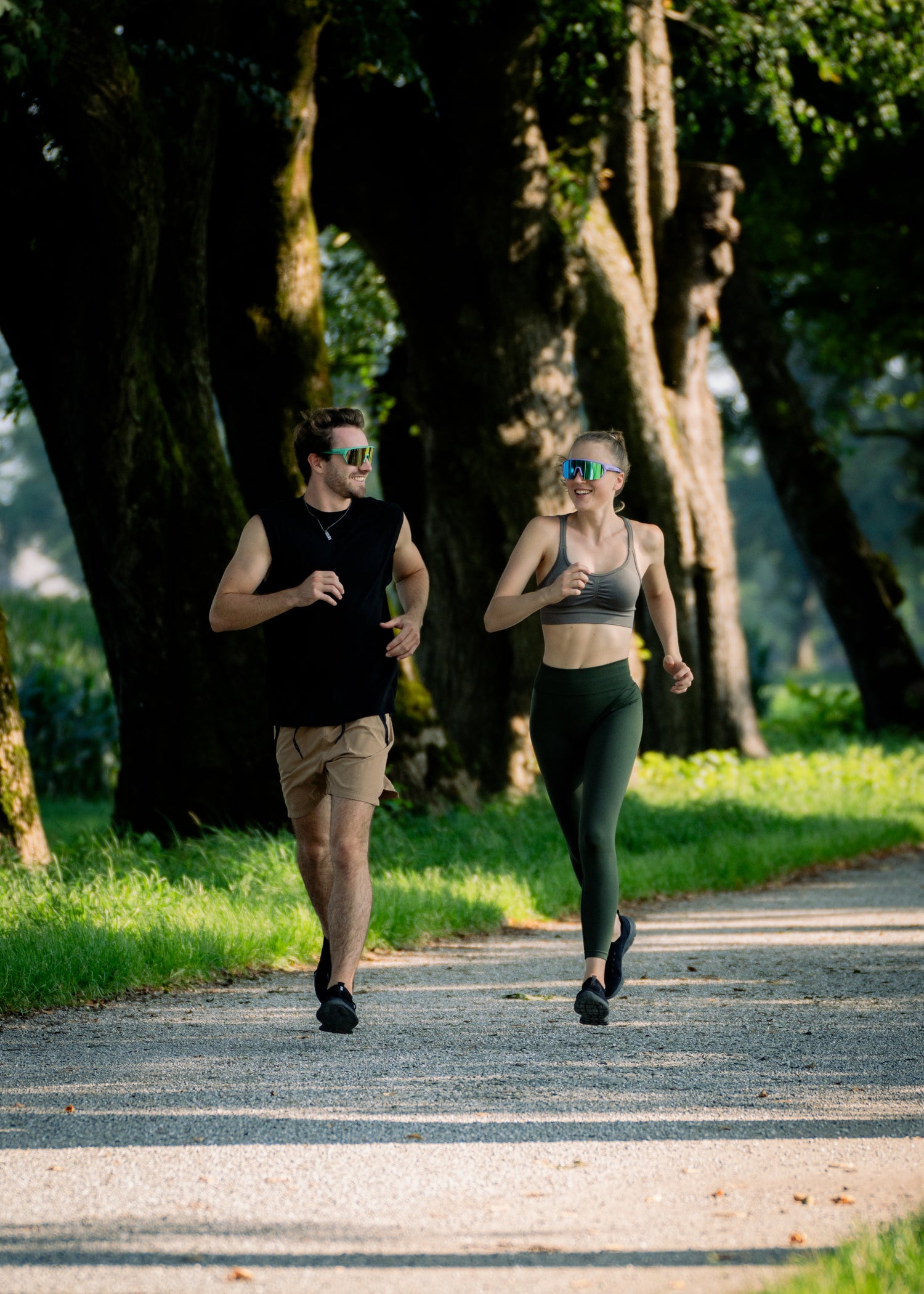Ein junges Paar läuft durch einen Wald auf einer Schotterstraße, sie tragen beide bunte Laufbrillen; Credits: Elias Neier