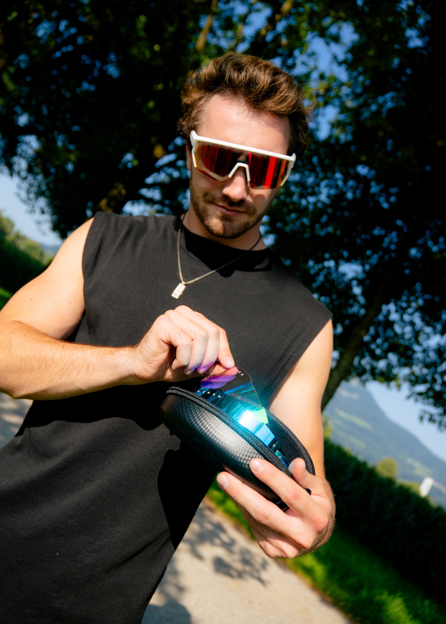 Ein Mann steht in der Natur und hält Sportbrillen Case in der Hand und zeigt die verscheidenen Gläser seiner Laufbrille; Credits: Elias Neier