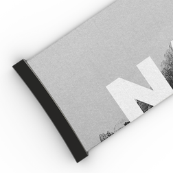 Eine Nahaufnahme einer grauen Matte mit schwarzem Rand und einem großen weißen Buchstaben „N“, der teilweise auf der Oberfläche zu sehen ist; die Textur ähnelt der des hochwertigen NAKED Optics Extra Strap (45 mm), der für die Brillenmodelle FORCE EVO, TROOP EVO, STORM, NOVA, SOLAR und ZEND entwickelt wurde.