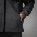A person wearing the dark Fleece Jacke - Thermiq from NAKED Optics with one hand in the pocket, standing against a gray background. This windabweisende and wasserabweisende jacket combines comfort with reliable protection from the elements.