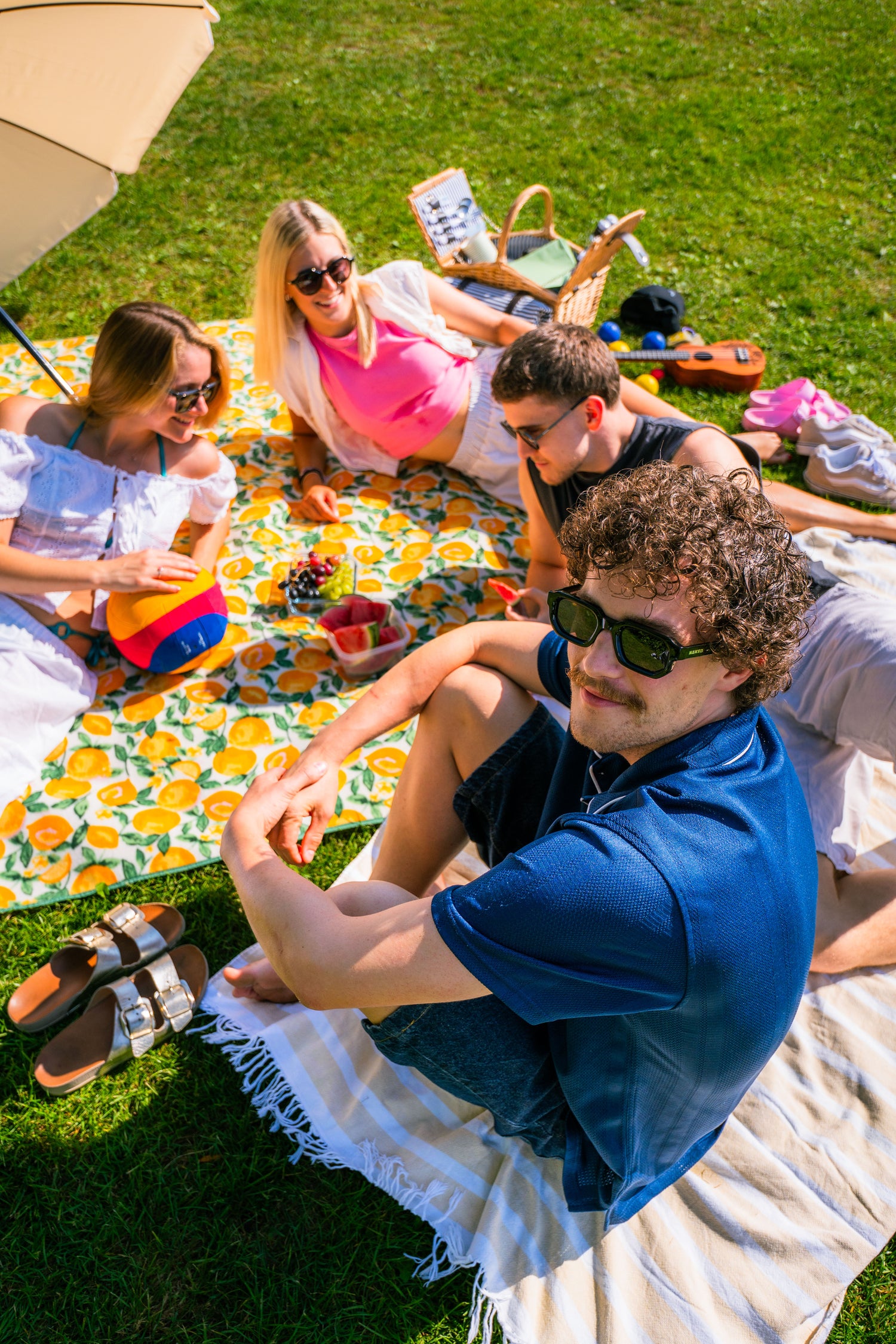 Eine Gruppe Freunde sitzt mit bunten Sonnnenbrillen auf einer Picknickdecke;  Credits: Elias Neier
