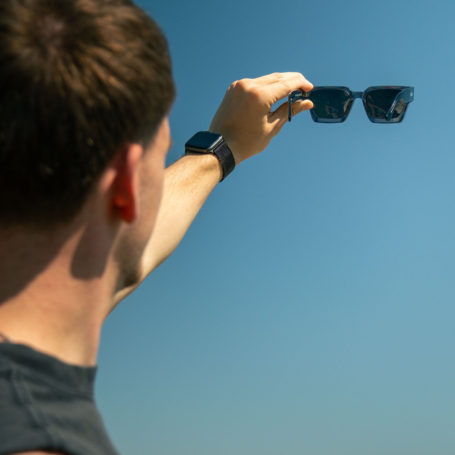 Ein Mann hält eine Sonnenbrille in den Himmel und zeigt den UV Schutz der Brille; Credits: Elias Neier