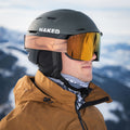 Ein Mann in einer braunen Jacke und einem Skihelm mit verspiegelter Skibrille steht auf einem verschneiten Berg, den Blick nach links gerichtet. Er trägt „The NOVA“ von NAKED Optics, eine große Skibrille mit Antibeschlagbeschichtung, die unter allen Bedingungen für klare Sicht sorgt.
