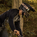 A person wearing a full-face helmet and black jersey, equipped with NAKED Optics The ZEND MTB Brille featuring magnetische Wechselgläser, rides a mountain bike in a forested area.