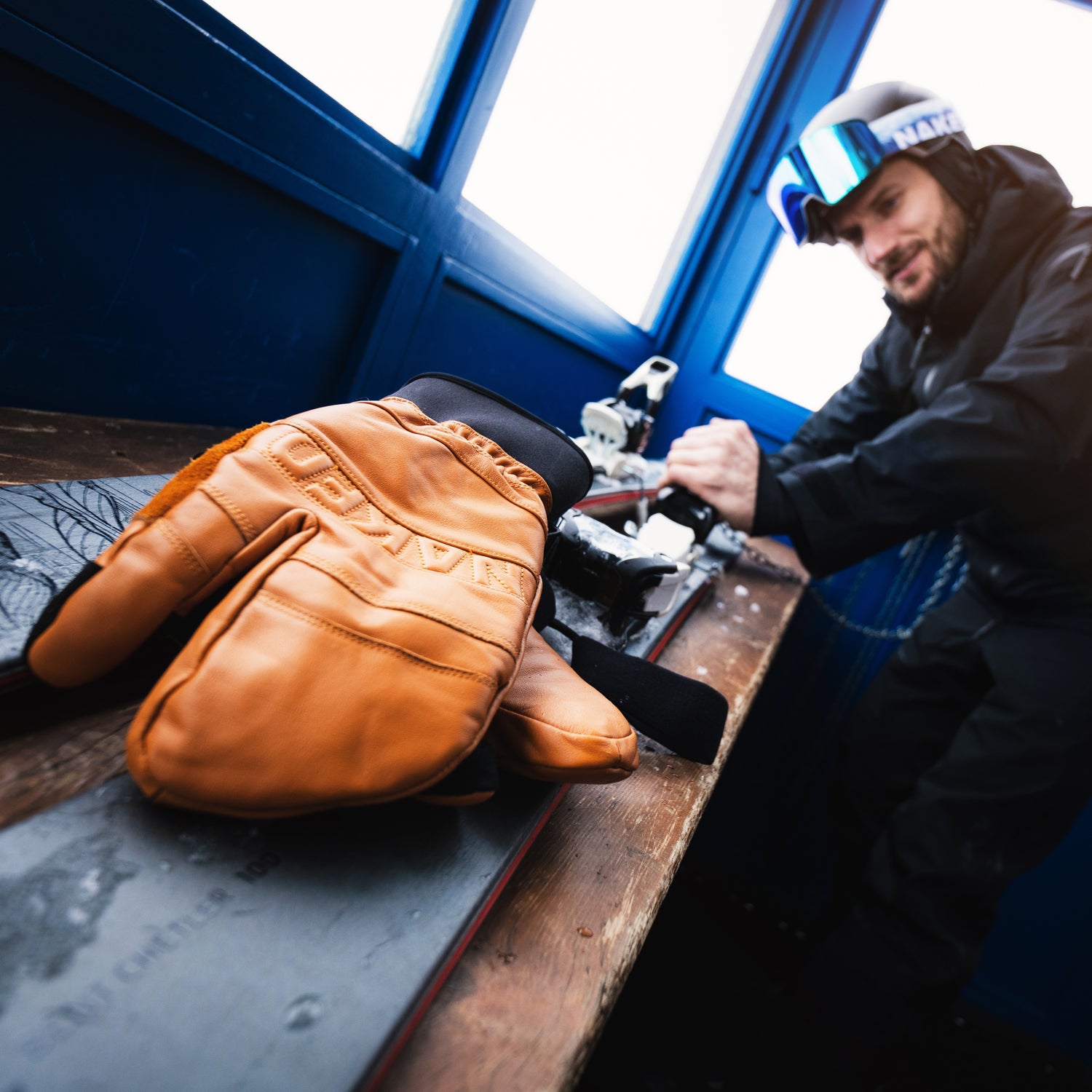 Ein Skifahrer stellt seine Skibindung ein, im Vordergrund des Bildes liegen Skihandschuhe; Credits: Elias Neier