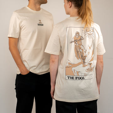Zwei Personen in cremefarbenen NAKED Optics T-Shirts; eines zeigt eine Tarot Design Biker-Illustration mit dem Text THE FOOL auf dem Rücken.