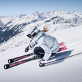 Ein Skifahrer in einer weißen Jacke saust unter strahlend blauem Himmel die verschneiten Berge hinunter und trägt dabei die Hochleistungs-Skibrille TROOP EVO von NAKED Optics mit Anti-Fog-Beschichtung für kristallklare Sicht.
