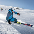 Frase riscritta: Uno sciatore in tenuta blu, che indossa gli occhiali TROOP EVO di NAKED Optics con rivestimento antiappannamento, scende a tutta velocità lungo un pendio innevato in una giornata di sole.