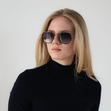 Eine Frau mit langen blonden Haaren, die eine NAKED Optics Sonnenbrille mit UV400-Schutz und einen schwarzen Rollkragenpullover trägt, schaut zur Seite und verkörpert einen urbanen Lifestyle.