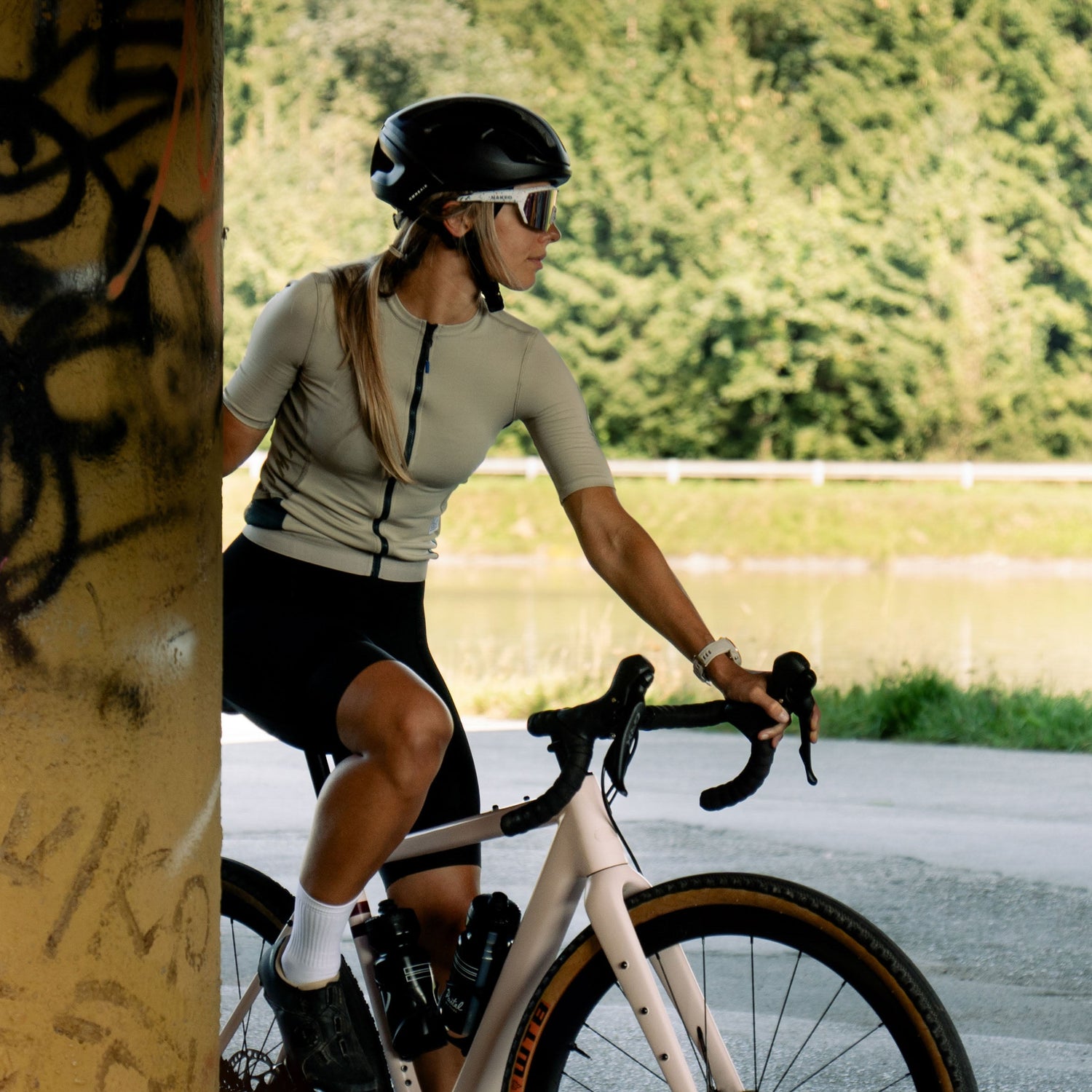 Eine Fahrradfahrerin lehnt an einer Mauer, mit iherer weißen Fahrradbrille schaut sie in die Ferne; Credits: Elias Neier