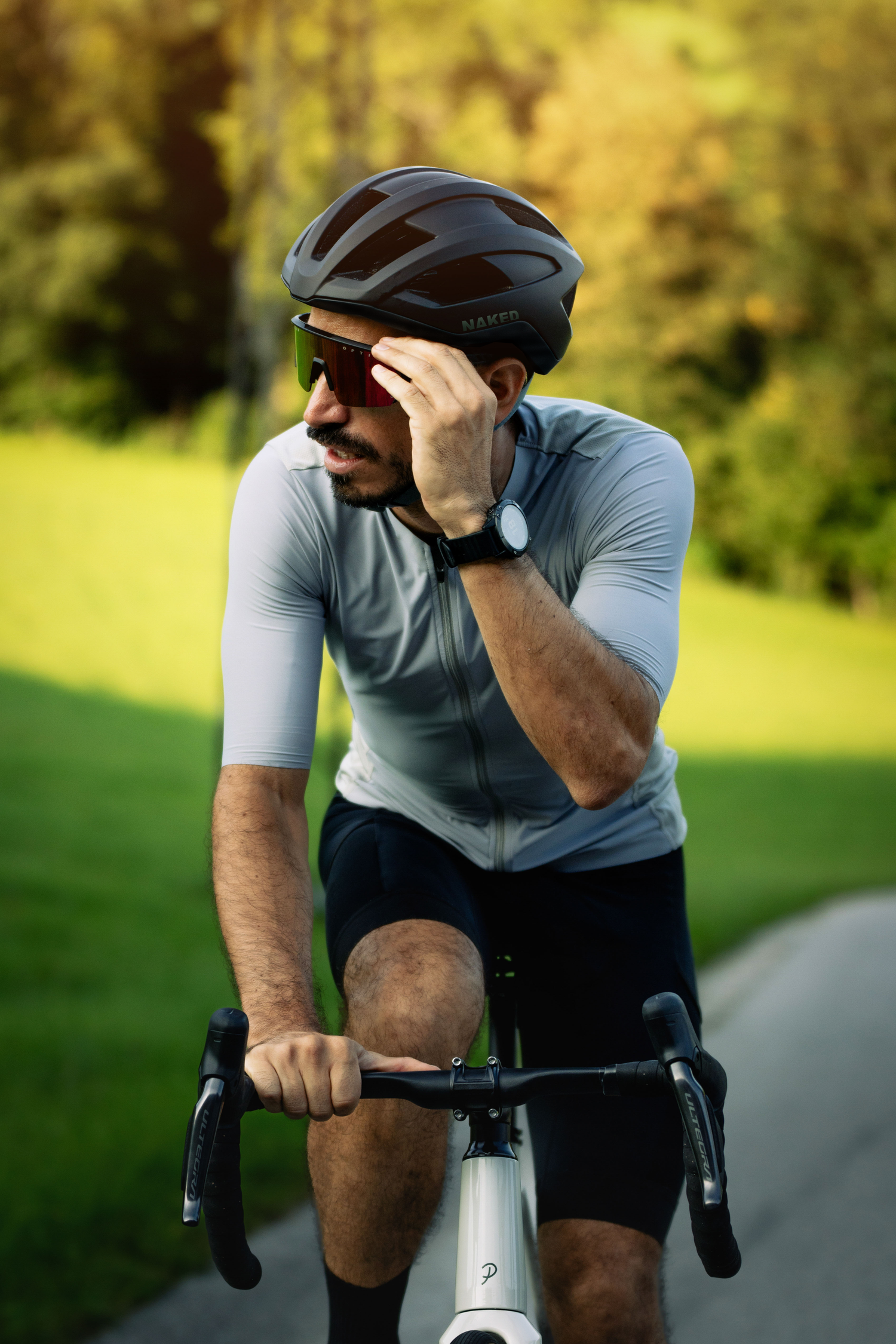 Ein Mann auf einem Fahrrad setzt sich seine Fahrradbrille auf und trägt einen Rennradhelm; Credits: Elias Neier