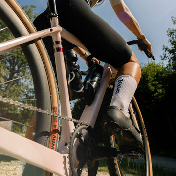 Nahaufnahme eines Radfahrers, der an einem sonnigen Tag im Freien mit einem Schotterfahrrad unterwegs ist, wobei seine Beine in stylischen Fahrradsocken und dem NAKED Optics Fahrradrahmen zur Geltung kommen.