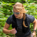 Runner wearing white NAKED Optics RAVE sports sunglasses on a wooded trail.