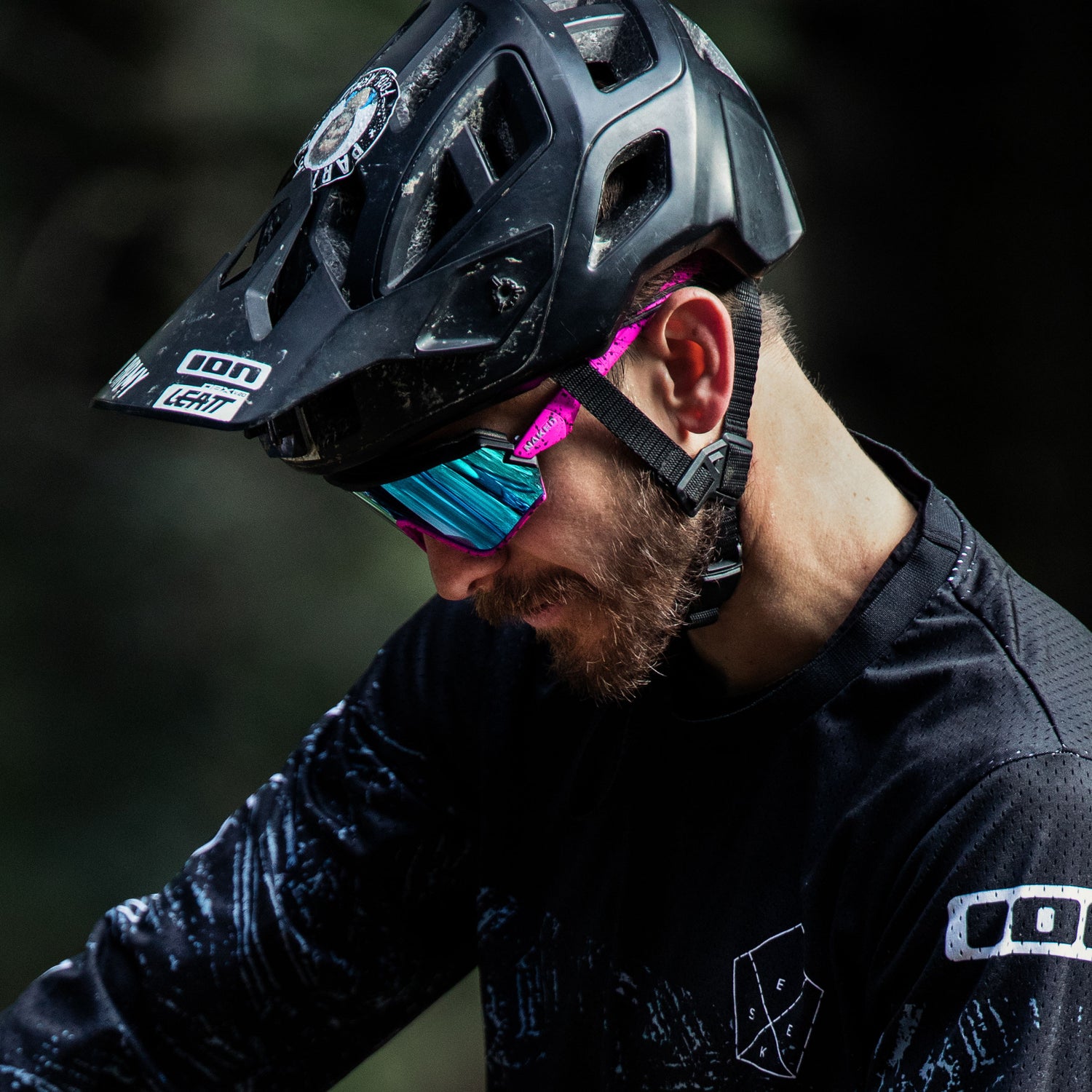 Ein Radfahrer, der einen schwarzen Helm und eine NAKED Optics Sportbrille klein mit reflektierenden Gläsern trägt, schaut im Freien nach unten.