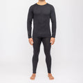 Una persona è in piedi a piedi nudi su uno sfondo bianco e indossa una maglia a maniche lunghe e dei leggings grigio scuro abbinati, della collezione NAKED Optics Thermo-Unterwäsche Herren (100% lana merino).