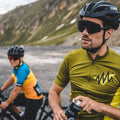 Zwei Radfahrer mit Helm und der FALCON Sportsonnenbrille von NAKED Optics machen auf einer Bergstraße eine Pause; einer von ihnen hält eine Wasserflasche in der Hand. Ihre Sportbrillen mit UV400-Schutz von NAKED Optics schützen ihre Augen vor der Sonne und sorgen so während der gesamten Fahrt für klare Sicht und maximalen Schutz.